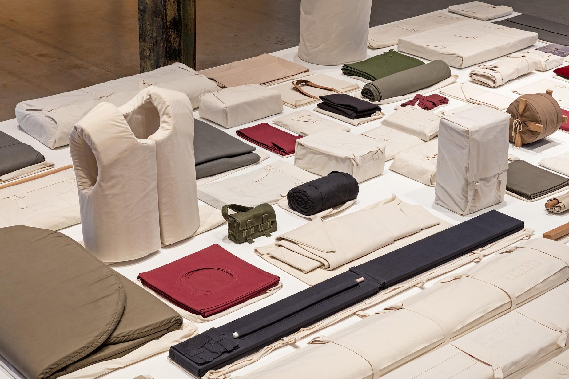 Folded, rolled and sewn fabric objects of 1. Werksatz laid out in rows on a long white table
