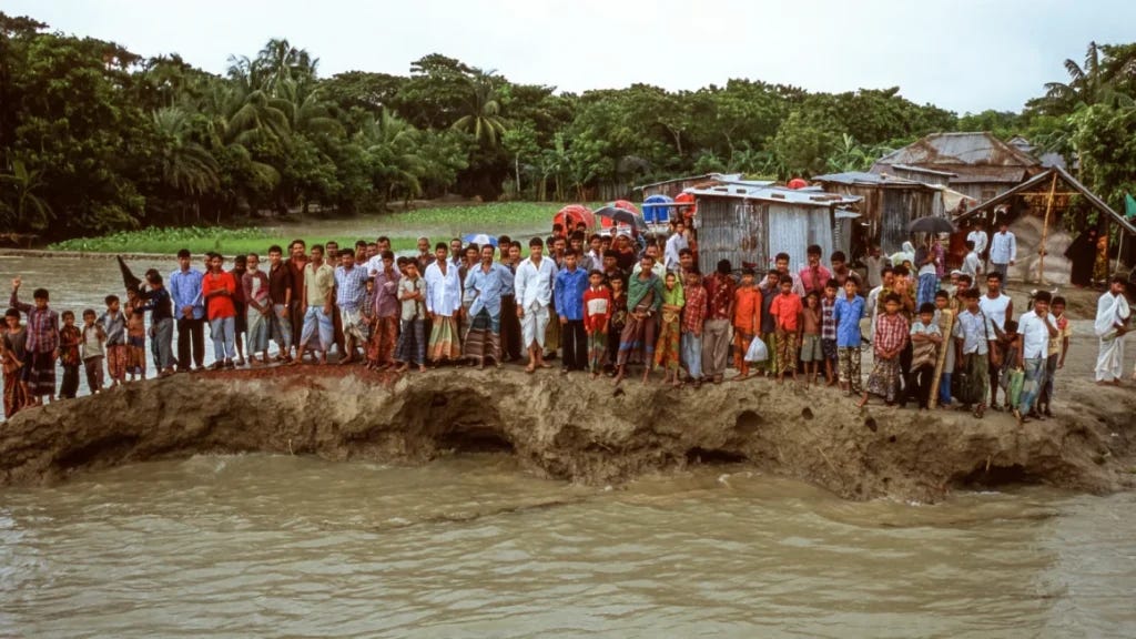 Villagers stand on a remnant of a road in Bhola Island, Bangladesh, in 2005. The area, at the mouth of the Ganges delta, is still suffering from accelerated erosion due to sea level rise. ©Gary Braasch